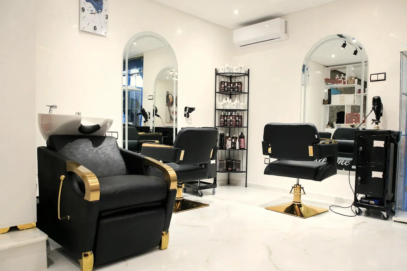 Le salon de coiffure d'Elle One, fauteuils noirs aux pieds dorés, miroirs en arche et sol en marbre